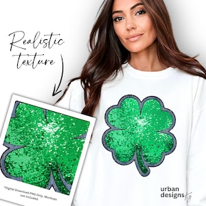May include: A white sweatshirt with a green four-leaf clover made of sequins. The clover is outlined in blue. The text "urban designs ky" is printed on the bottom right corner of the sweatshirt.