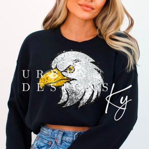 May include: Black cropped sweatshirt with a sequined eagle design. The eagle has a white head and body with gold beak and eyes. The text "Urban Designs Ky" is written in white cursive on the bottom right corner of the sweatshirt.