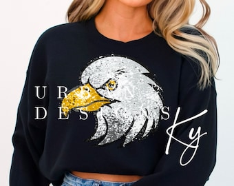 May include: Black cropped sweatshirt with a sequined eagle design. The eagle has a white head and body with gold beak and eyes. The text "Urban Designs Ky" is written in white cursive on the bottom right corner of the sweatshirt.