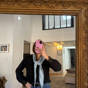May include: A black long-sleeve sweater with lace cuffs and a light blue scarf. The person is wearing blue jeans and a black belt. The mirror has a gold ornate frame.