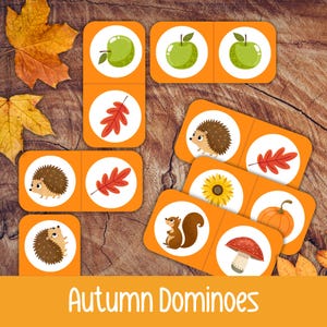 May include: A set of orange dominoes featuring illustrations of green apples, red oak leaves, hedgehogs, a sunflower, a squirrel, a pumpkin, and a mushroom. The game pieces are arranged on a wooden surface with scattered autumn leaves.
