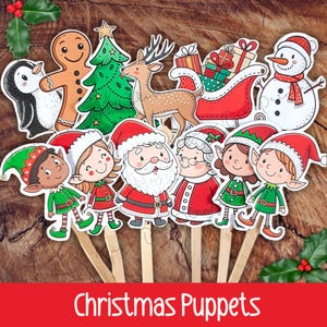 Puede incluir: Un conjunto de marionetas navideñas sobre palos de madera. Las marionetas incluyen a Papá Noel, Mamá Noel, elfos, un muñeco de nieve, un reno, un árbol de Navidad, un hombre de jengibre, un pingüino y un trineo. El texto "Christmas Puppets" está en la parte inferior.