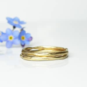 Könnte beinhalten: Zwei goldene Ringe, die übereinander liegen. Die Ringe sind aus strukturiertem Metall und haben eine leicht unregelmäßige Form.