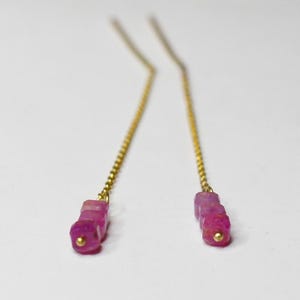 Könnte beinhalten: Ein Paar zarte goldene Kettenohrringe mit rosafarbenen Edelstein-Akzenten. Die Ohrringe haben einen Cluster aus kleinen, quadratischen rosafarbenen Edelsteinen.