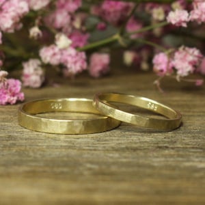 Könnte beinhalten: Zwei goldene Eheringe mit gehämmerter Oberfläche. Die Ringe liegen übereinander.