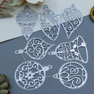 Może przedstawiać: Zestaw dziewięciu metalowych wykrojników do ozdób choinkowych. Ozdoby mają kształt dzwonków, gwiazd i łez. Ozdoby są wszystkie ozdobione misternymi wzorami i spiralami.