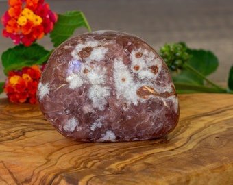 May include: A smooth, polished, purple and white agate stone with brown inclusions. The stone is shaped like a rounded oval and has a natural, organic look.