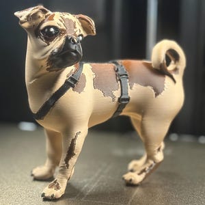Könnte beinhalten: Eine hellbraune und braune Mops-Figur mit schwarzem Geschirr. Der Mops hat ein abgenutztes Aussehen mit dunkleren braunen Flecken auf Rücken und Kopf. Die Figur steht und zeigt ihre kurzen Beine und den eingerollten Schwanz.