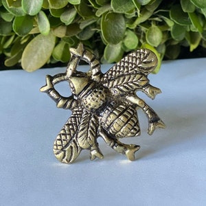 May include: A gold-toned metal bee napkin ring with intricate details. The bee has a textured body and wings.