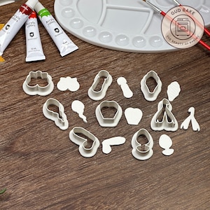 Könnte beinhalten: Ein Set mit 15 weißen Plastik-Ausstechern in verschiedenen Formen, darunter ein Herz, ein Stern, eine Blume, ein Ballon und eine Karotte. Die Ausstecher sind auf einer Holzoberfläche angeordnet.