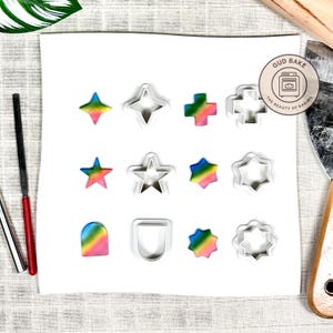 Könnte beinhalten: Eine Auswahl an Metall-Ausstechern in Stern-, Kreuz- und anderen Formen, zusammen mit Regenbogenfarbenem Ton. Die Ausstecher sind silberfarben. Das Bild enthält ein Logo mit der Aufschrift "GUD BAKE THE BEAUTY OF BAKING".