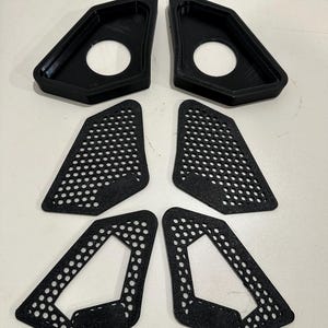 May include: A set of six black, geometric automotive parts. Two pieces have a solid, triangular shape with a circular opening. The other four pieces are triangular with a perforated dot pattern.