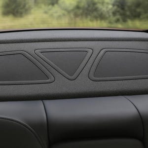 Pode incluir: Detalhe interior do carro com uma prateleira traseira preta com três capas de alto-falantes. As capas dos alto-falantes têm formas de diamante e triângulo. Abaixo, um assento de carro de couro preto.