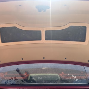 Pode incluir: Vista interior da mala de um carro com um painel de madeira personalizado. O painel tem uma moldura de madeira clara e duas inserções retangulares escuras. O interior da mala é bege e o exterior do carro é vermelho.