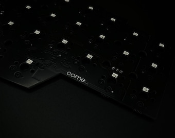 May include: Close-up of a black circuit board with numerous small, square LED lights. The board has a complex pattern of circuits and components, with the word "corne" printed on it. The overall aesthetic is dark and technical.
