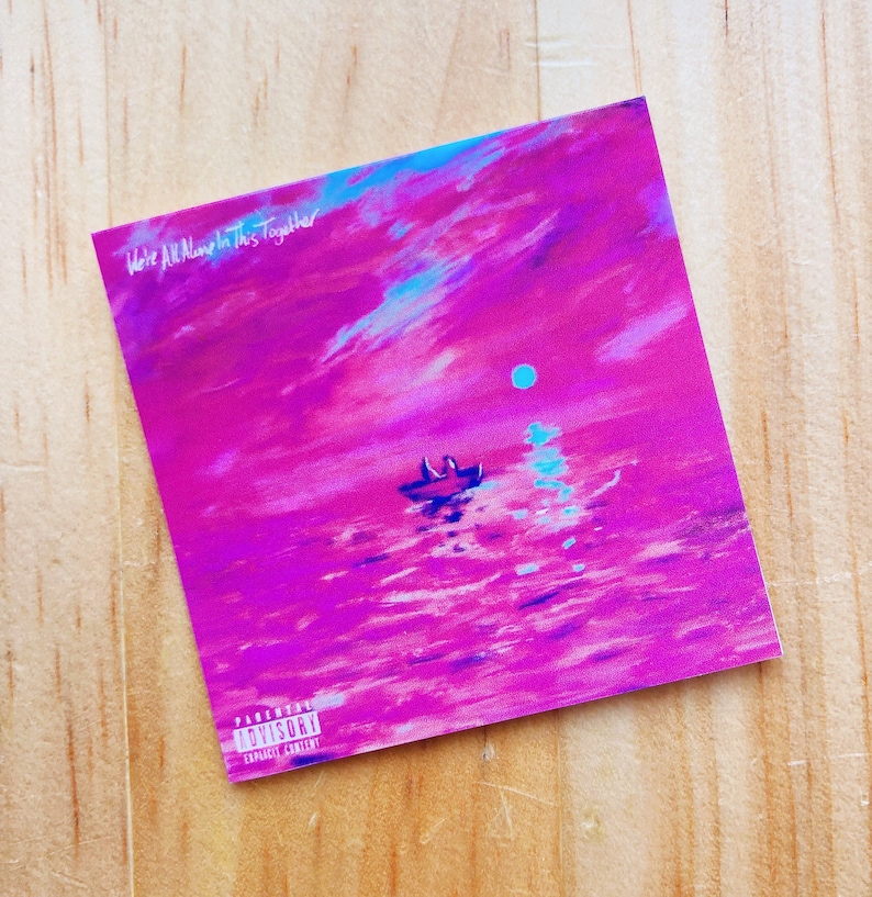 May include: Square print featuring a vibrant, surreal landscape in shades of pink, purple, and blue. A small boat floats on water under a sky with a moon. Text at the top reads "We're All Alone In This Together."