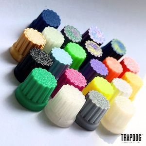 Puede incluir: Una colección de objetos cilíndricos coloridos con tapas texturizadas. Los objetos son de varios colores, incluyendo verde, rosa, amarillo y azul. Los objetos están dispuestos en un patrón diagonal sobre un fondo blanco.