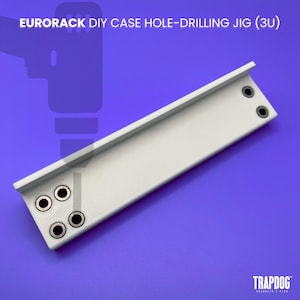 May include: A white Eurorack DIY case hole-drilling jig with four pre-drilled holes and two additional holes. The text "EURORACK DIY CASE HOLE-DRILLING JIG (3U)" is at the top. The brand name "TRAPDOG" is at the bottom.