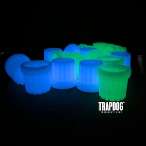 Peut inclure: Un ensemble d'objets cylindriques brillants, bleus et verts, sur fond noir. Les objets ont une surface textur&eacute;e et &eacute;mettent une lumi&egrave;re interne douce. Le texte "TRAPDOG" est visible en bas, avec le slogan "PRODUCER'S PLUGS".
