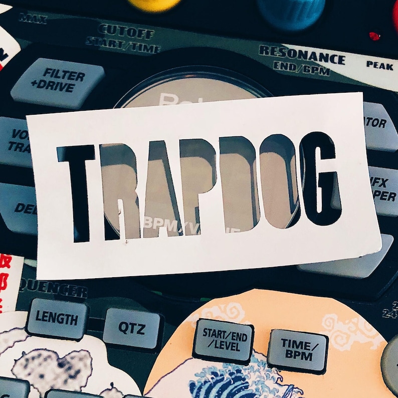 Peut inclure: Un pochoir blanc avec le mot "TRAPDOG" d&eacute;coup&eacute; est pos&eacute; sur un appareil de production de musique &eacute;lectronique noir. L'appareil comporte divers boutons et molettes avec des inscriptions telles que "CUTOFF", "FILTER" et "TIME/BPM". Le fond comprend des accents color&eacute;s.