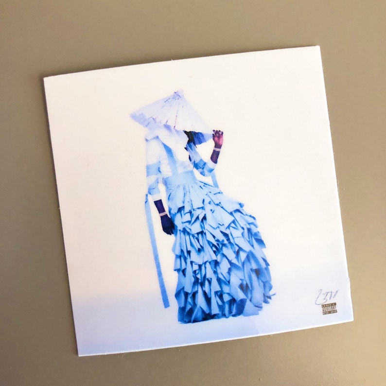 May include: A square print featuring a figure in a light blue dress with layered ruffles and a matching hat. The figure is set against a white background. The print has a minimalist aesthetic.