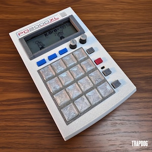 Puede incluir: Un dispositivo electrónico blanco y gris con el texto "PO2000XL" en la parte superior. Cuenta con una pantalla que muestra una imagen de dibujos animados, varios botones y una cuadrícula de teclas cuadradas. El dispositivo está sobre una superficie de madera.