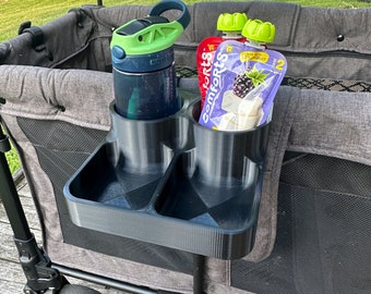 May include: A black 3D-printed wagon organizer with cup holders and a tray. It holds a blue water bottle with a green lid, and two pouches of baby food. The organizer is attached to a gray wagon.