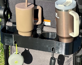 May include: A black stroller organiser with two cup holders, a straw cup, a travel mug, a small speaker, and a black pouch hanging from the side.