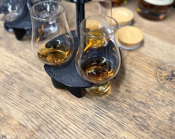 May include: A black metal stand with four glass whiskey tasting glasses filled with amber liquid. The stand is on a wooden barrel.