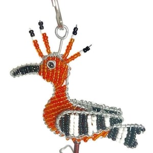 May include: A beaded wire bird keyring with orange, black and white beads. The bird has a long beak and a crown of beads on its head.