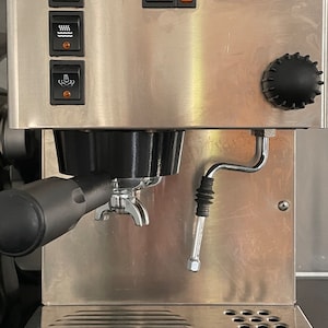 May include: A silver Rancilio espresso machine with a black portafilter and a steam wand. The machine has a variety of buttons and controls, including a power button, a steam button, and a hot water button.