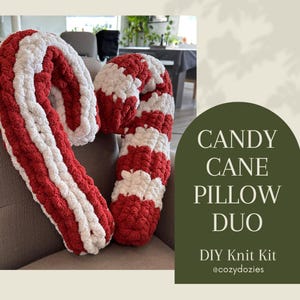 May include: Two candy cane-shaped pillows made of thick, chunky yarn with alternating red and white stripes. The text on the right side of the image reads: CANDY CANE PILLOW DUO, DIY Knit Kit, @cozydozies. The pillows have a soft, textured appearance.