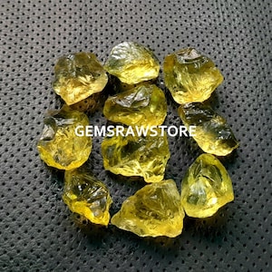 May include: A collection of ten yellow citrine rough stones. The stones are various sizes and shapes, with some having a more pointed shape and others being more rounded. The stones are all a bright yellow color.