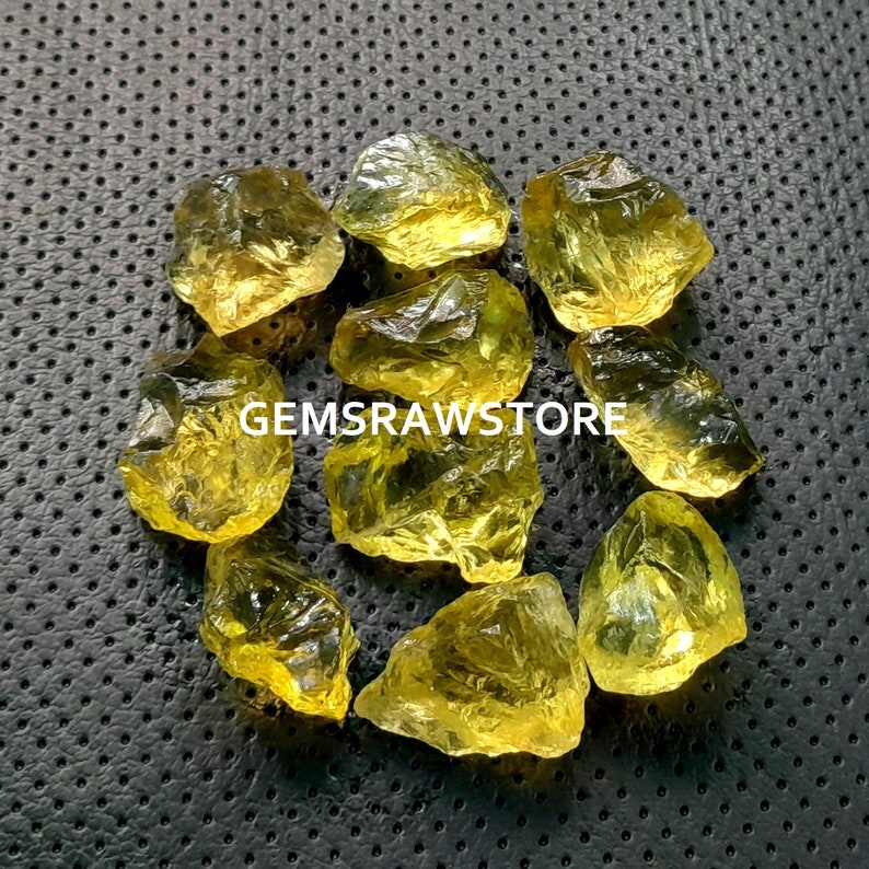 May include: A collection of ten yellow citrine rough stones. The stones are various sizes and shapes, with some having a more pointed shape and others being more rounded. The stones are all a bright yellow color.