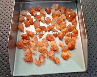 May include: A collection of small, rough, orange sunstone crystals in a metal tray. The crystals are various shapes and sizes.