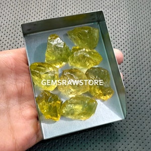 May include: A collection of yellow-green raw citrine crystals in a metal tray. The crystals are rough and have a natural, unpolished look.