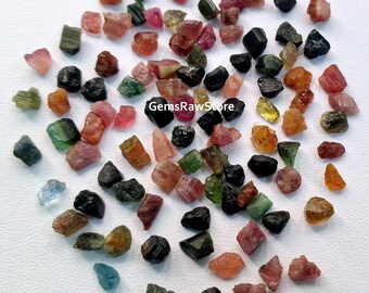 Könnte beinhalten: Eine Sammlung roher, unpolierter Edelsteine in verschiedenen Farben, darunter Grün, Rosa, Rot, Schwarz und Braun. Die Edelsteine sind klein und unregelmäßig geformt, und einige haben einen metallischen Glanz. Der Text "GemsRawStore" ist im Bild sichtbar.