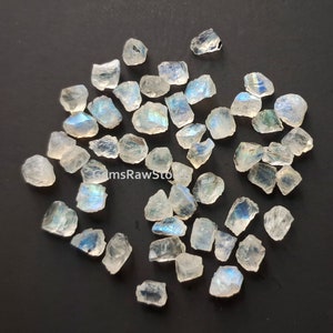 May include: A collection of iridescent moonstone rough, with a variety of shapes and sizes. The stones are a milky white color with a rainbow sheen.