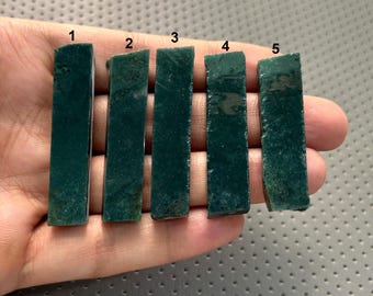 May include: Five rectangular, dark green stone slabs are displayed. Each slab has a slightly different texture and edge, with variations in the green hue. The stones are held in a hand, showcasing their individual characteristics.