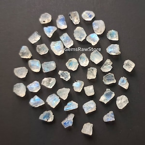 Puede incluir: Colección de cristales de piedra lunar en bruto, sin cortar, sobre una superficie oscura. Las piedras translúcidas muestran destellos azules y blancos. El texto "GemsRawStore" es visible en la imagen.