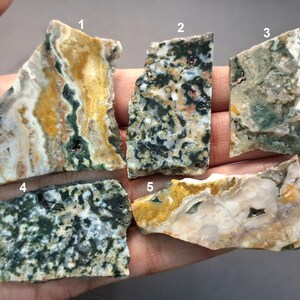 May include: Five irregularly shaped, polished stone slabs with unique patterns and colors. The stones display a variety of hues, including yellow, green, white, and black, with intricate veining and textures. Each piece is distinct, showcasing natural variations.