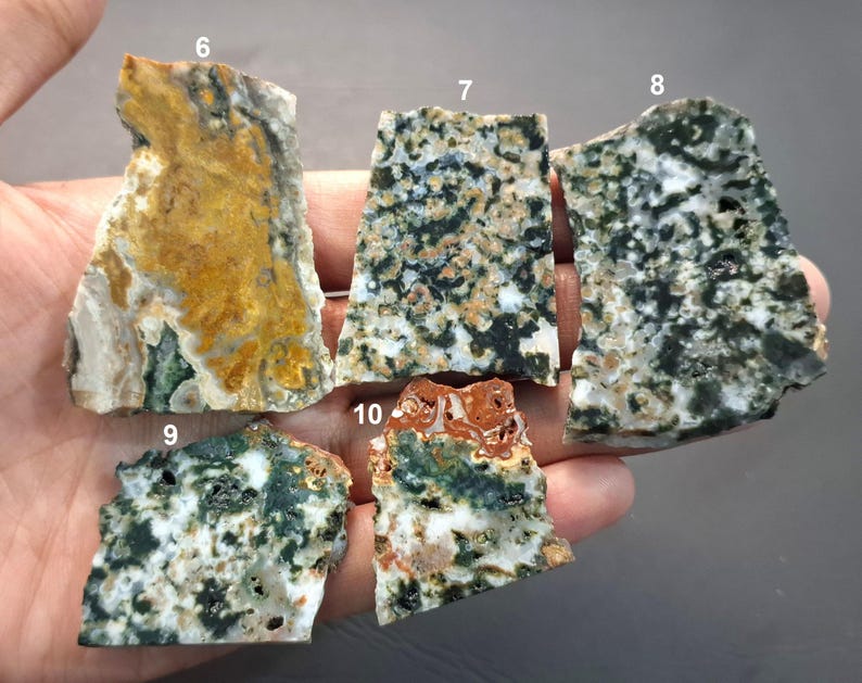 May include: A collection of five rough-cut, natural stone slabs. The stones display a variety of colors, including green, white, brown, and yellow. Each stone has a unique pattern and texture, showcasing the natural beauty of the material.
