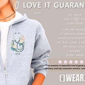 Pu&ograve; includere: Felpa con cappuccio grigia con chiusura a zip. La parte anteriore della felpa presenta uno stetoscopio con dettagli floreali e il testo "MEB". Il testo "LOVE IT GUARANTEE" &egrave; nella parte superiore dell'immagine. Il testo "ASH" &egrave; sotto il testo "LOVE IT GUARANTEE".