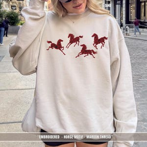 Sand light sweatshirt worn outdoors featuring maroon & black embroidered horse design