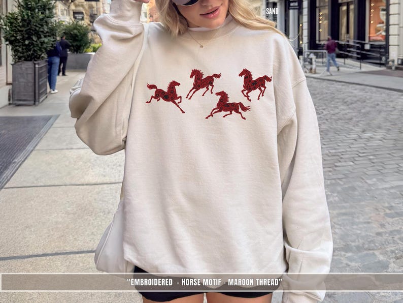 Sand light sweatshirt worn outdoors featuring maroon & black embroidered horse design