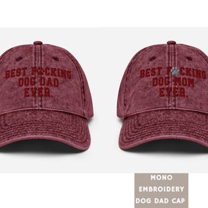 Peut inclure: Deux casquettes de baseball en toile rouge vieillie avec du texte brod&eacute;. La casquette de gauche dit "Best F*cking Dog Dad Ever." La casquette de droite dit "Best F*cking Dog Mom Ever."