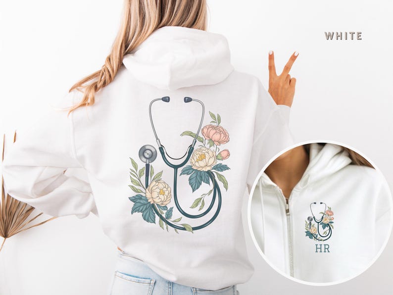 Pu&ograve; includere: Felpa con cappuccio bianca con un design floreale e uno stetoscopio sul retro. La felpa ha una cerniera e un cappuccio. Il testo "HR" &egrave; sul davanti della felpa.