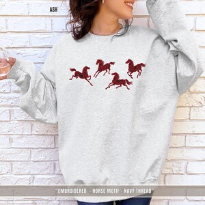 Ash grey unisex sweatshirt with maroon & black embroidered horse design shown in lifestyle setting