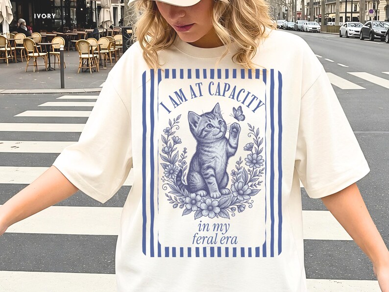 Funny Cat Lover Shirt on an Ivory Comfort Colors 1717 tee with an I Am at Capacity and in my feral era kitten design, shown in a casual streetwear mockup for introverts, cat moms, college students, and funny friend gifts.