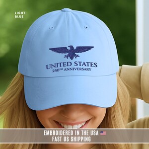 Light blue embroidered United States 250th anniversary baseball cap with eagle emblem, worn outdoors in natural light.